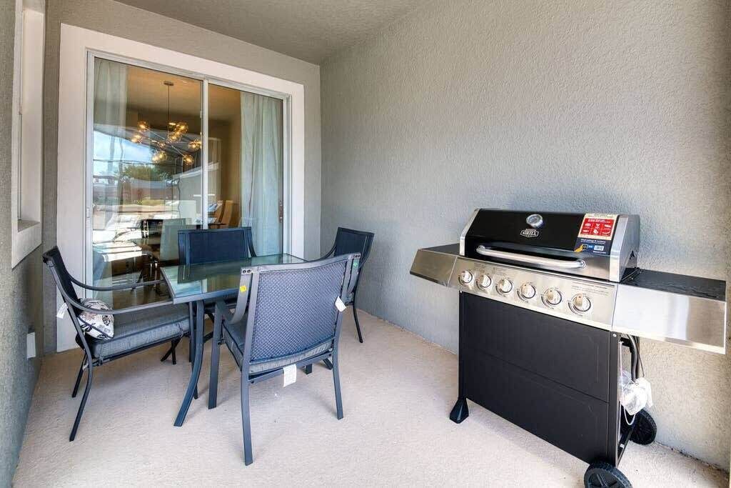 Un balcon avec une table et des chaises en verre, un barbecue et une vue sur un immeuble.