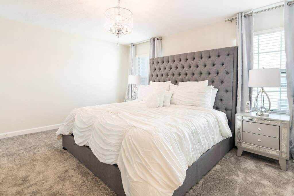 A bedroom with a tufted headboard, a large bed with white bedding, a nightstand with a lamp, and a window with curtains.