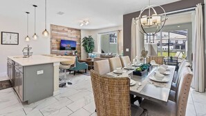 A modern kitchen with a central island, a dining area with a table set for four, and a living area with a sofa and TV. - Amazing Resort Near Disney 4BR Townhome (Kissimmee)