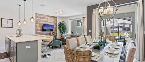 A modern kitchen with a central island, a dining area with a table set for four, and a living area with a sofa and TV.