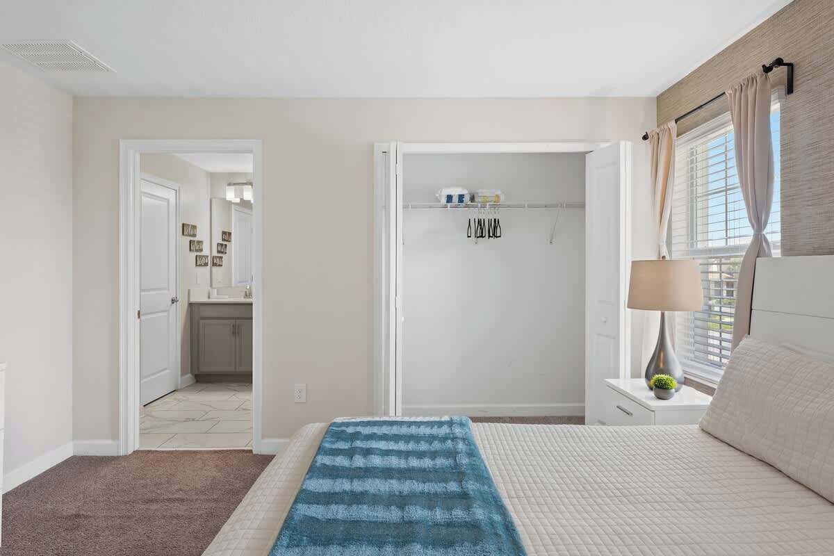 A bedroom with a bed, a nightstand, a lamp, a window with curtains, and a closet with a door.