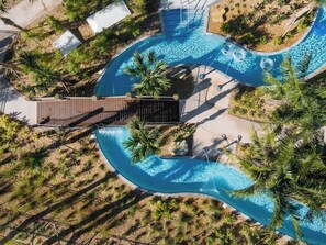 An aerial view of a resort with a large, winding swimming pool surrounded by palm trees and a wooden deck area. - Amazing Resort Near Disney 4BR Townhome (Kissimmee)