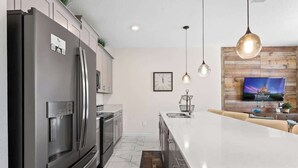 A modern kitchen with a large island, stainless steel appliances, pendant lighting, and a wooden accent wall. - Amazing Resort Near Disney 4BR Townhome (Kissimmee)