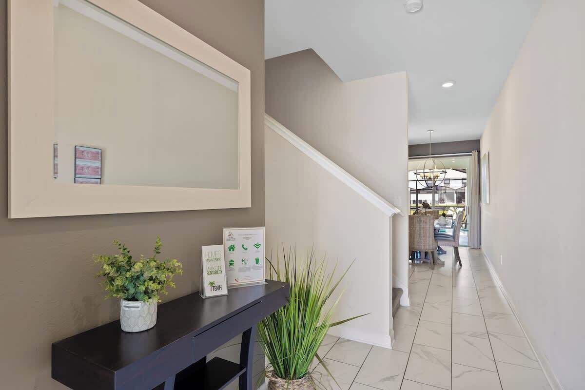 Un espace d’accueil moderne avec une console sombre, un miroir encadré et une plante en pot. Un escalier mène à une salle à manger située au fond de la pièce.