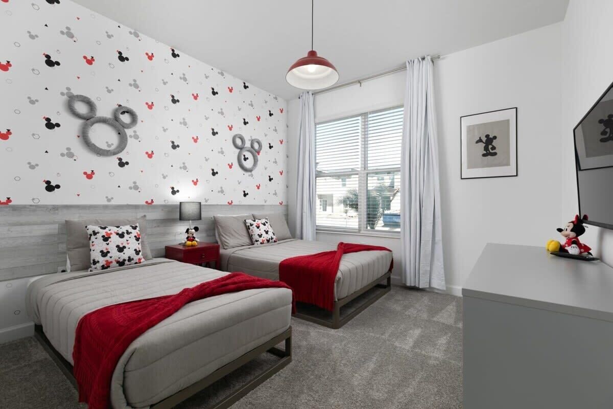 Een slaapkamer met twee bedden, een dressoir en een muur met een Mickey Mouse thema.