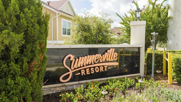 A sign for Summerville Resort with a clear view of the surrounding greenery and a residential building in the background.