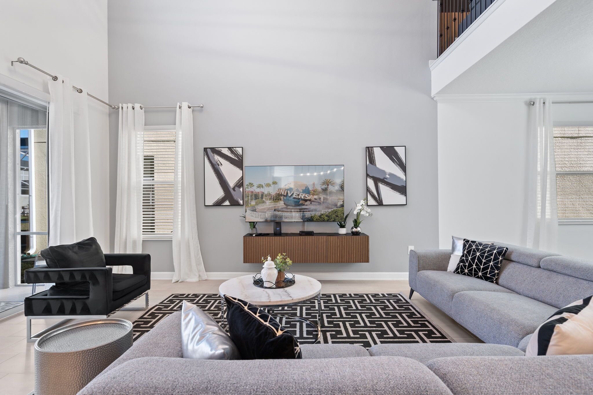 Ein modernes Wohnzimmer mit einem Flachbildfernseher, grauen Sofas, einem Couchtisch und einem gemusterten Teppich.