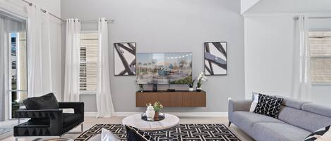 Ein modernes Wohnzimmer mit einem Flachbildfernseher, grauen Sofas, einem Couchtisch und einem gemusterten Teppich.