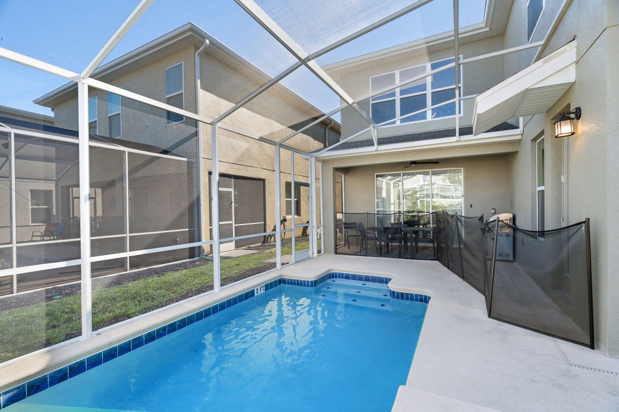 A swimming pool with a glass enclosure, a patio area with outdoor furniture, and a view of a house.