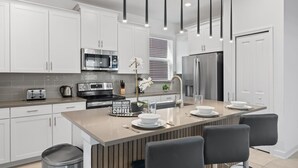 A modern kitchen with white cabinets, stainless steel appliances, a central island with bar seating, and pendant lighting. - Chic 5bed Retreat, Perfect for Family Getaways (Kissimmee)