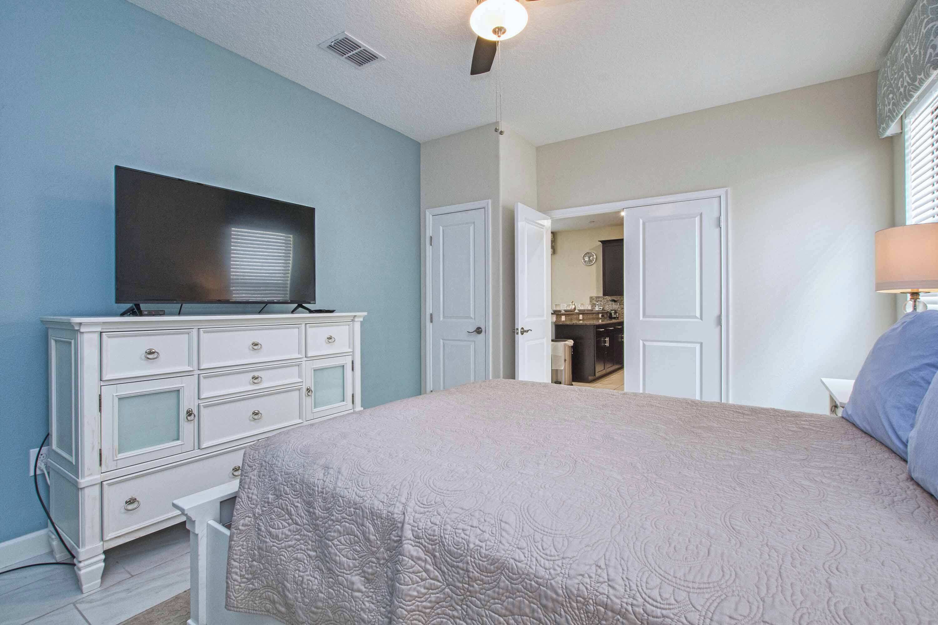 Une chambre à coucher comprenant un lit, une commode, un téléviseur et une porte donnant sur une salle de bain.
