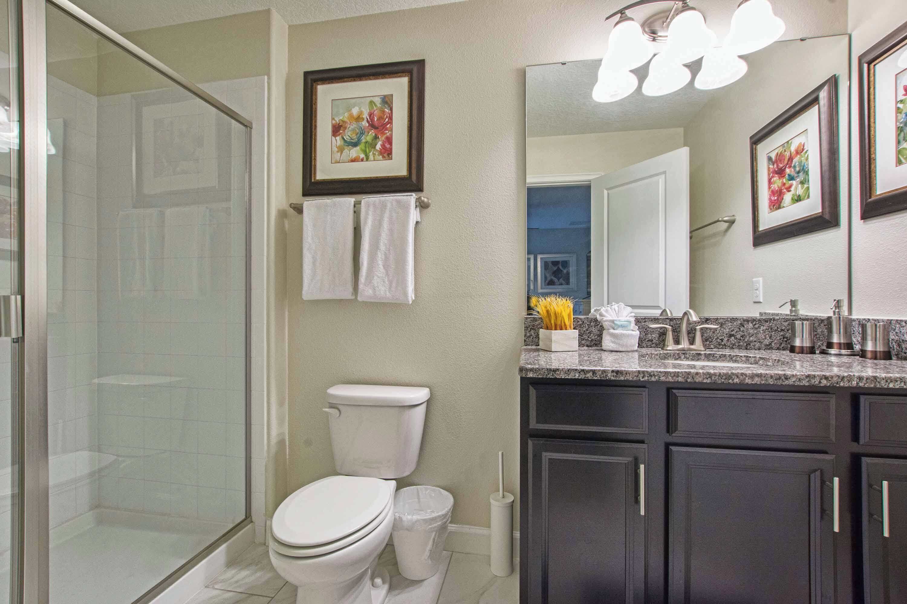 A bathroom with a glass-enclosed shower, a toilet, and a vanity with dark cabinets and a countertop.