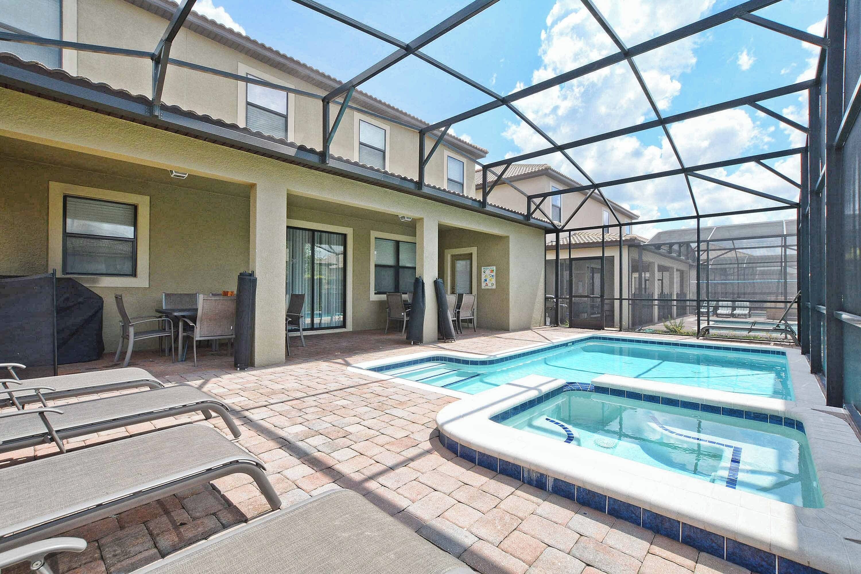A pool area with lounge chairs, a covered seating area, and a glass-enclosed structure.