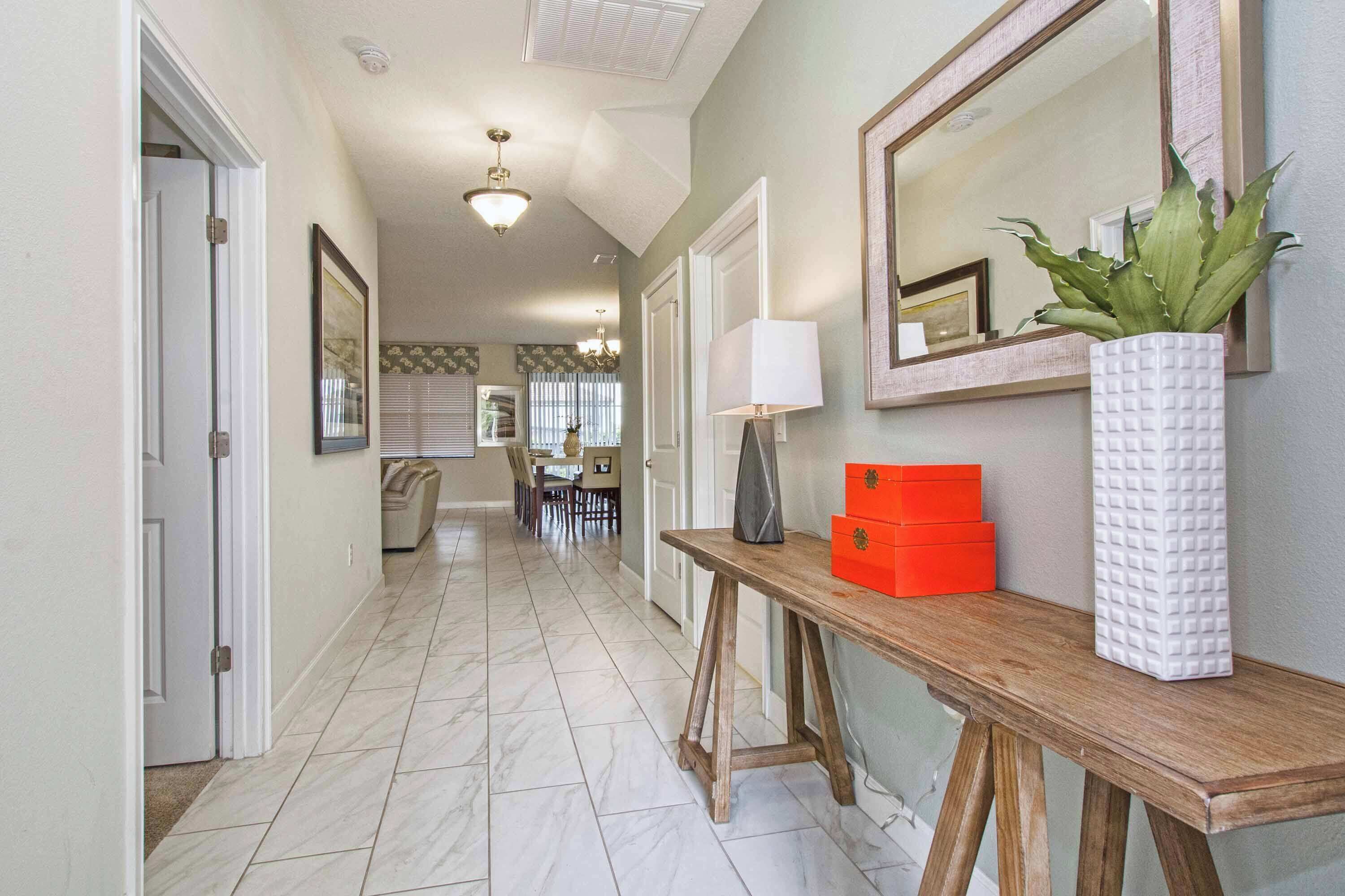 A hallway with a wooden console table, a white vase with a plant, and a mirror on the wall.