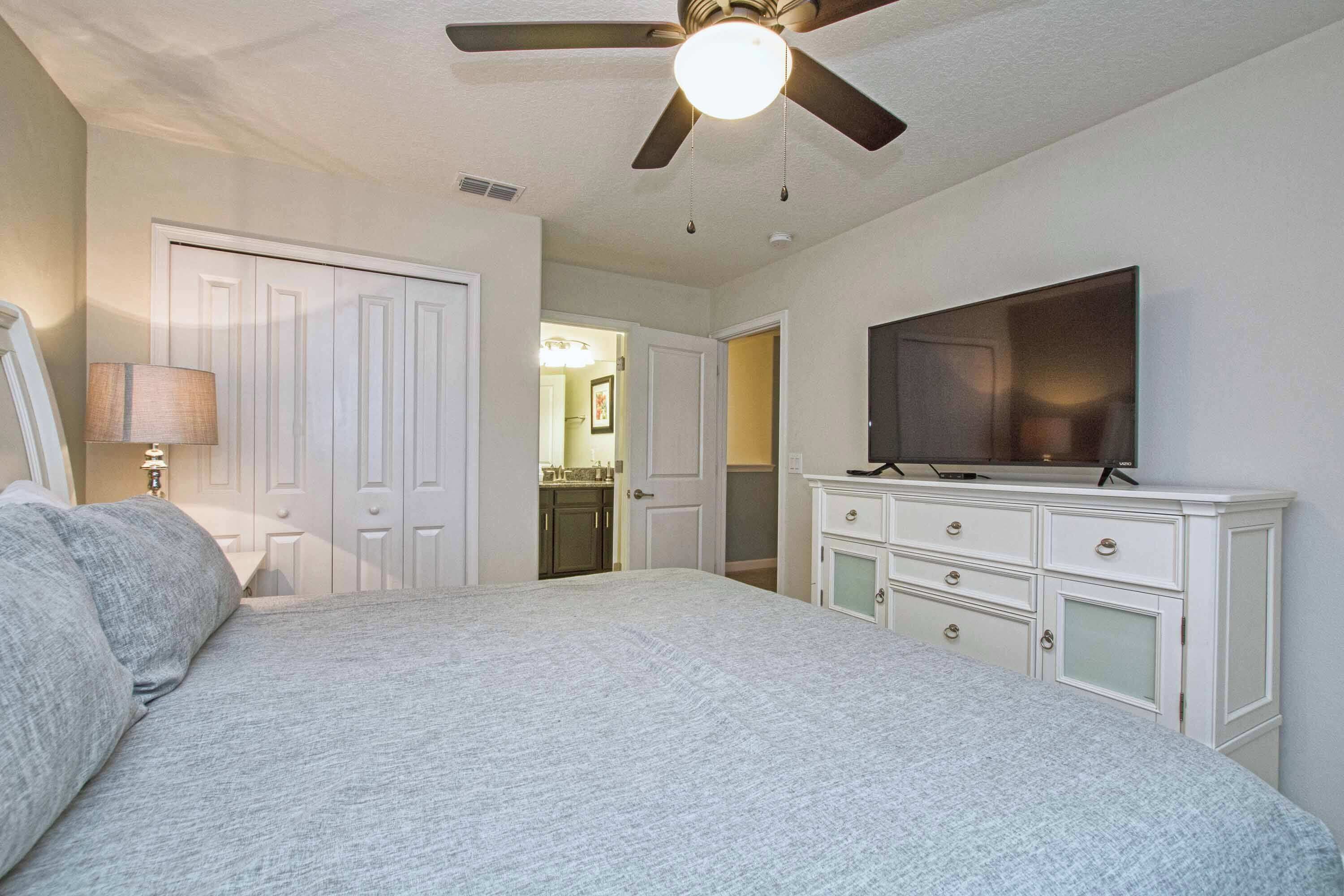 A bedroom with a bed, a dresser, a television, and a ceiling fan.