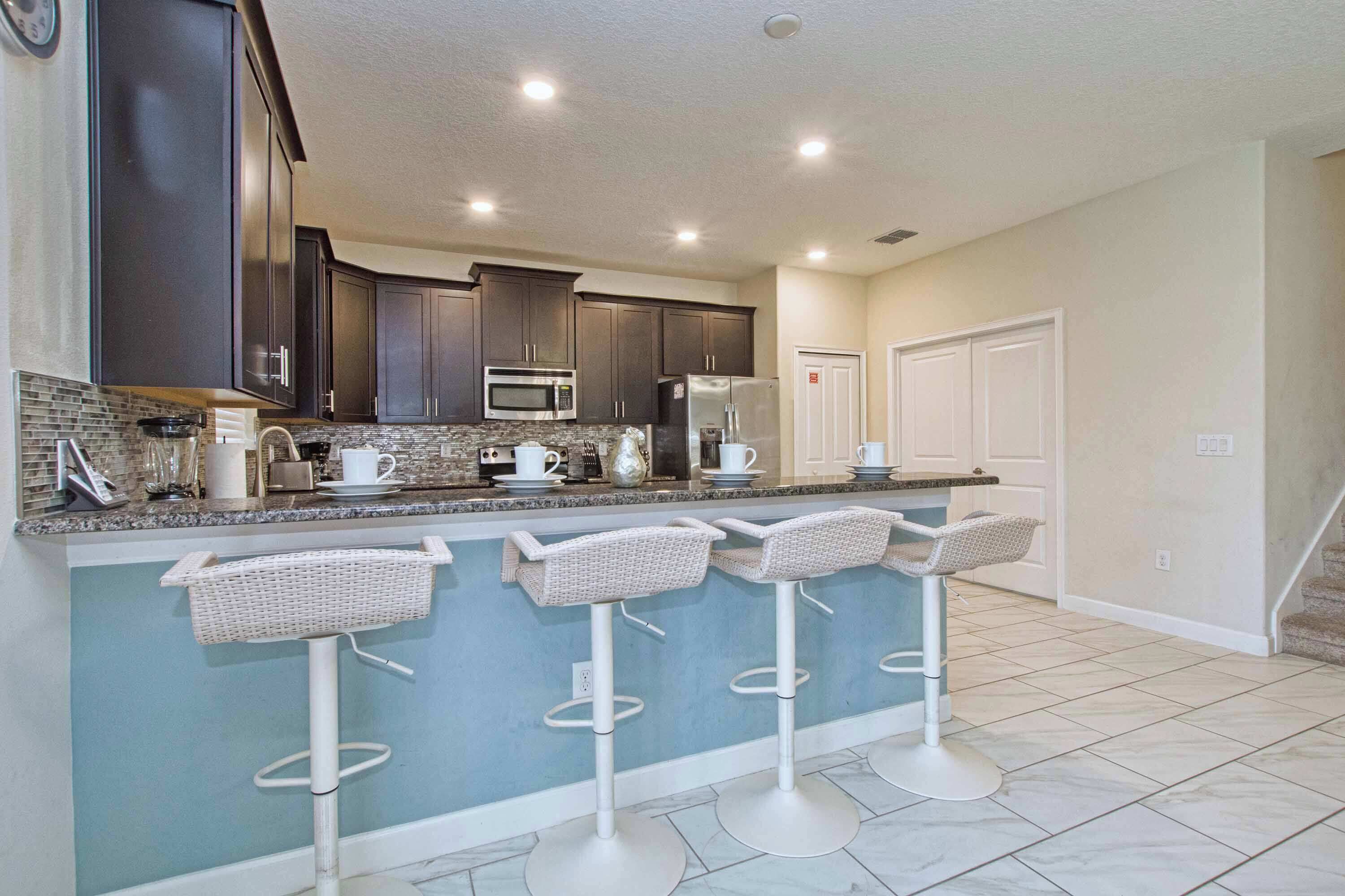 A modern kitchen with dark cabinets, a microwave, a refrigerator, and a bar area with white stools.