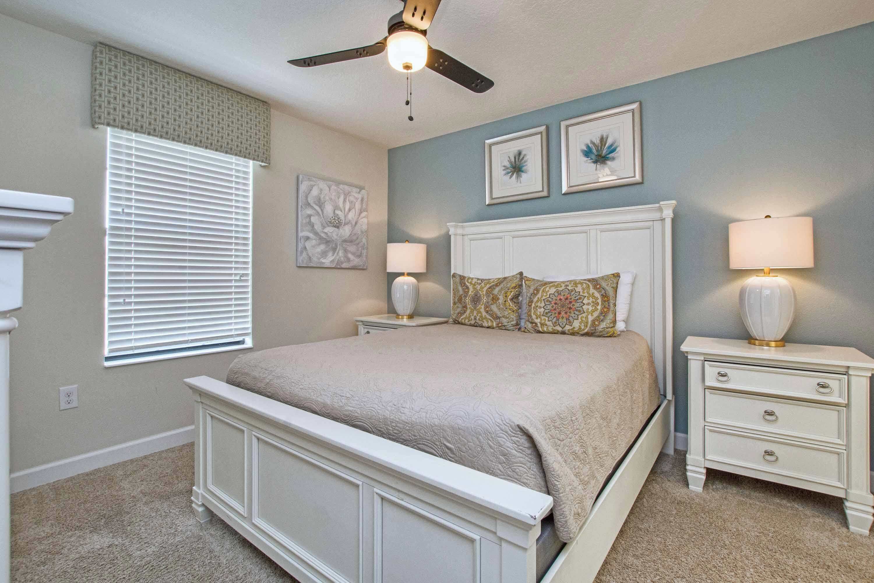 A bedroom with a bed, nightstands, a ceiling fan, and wall art.