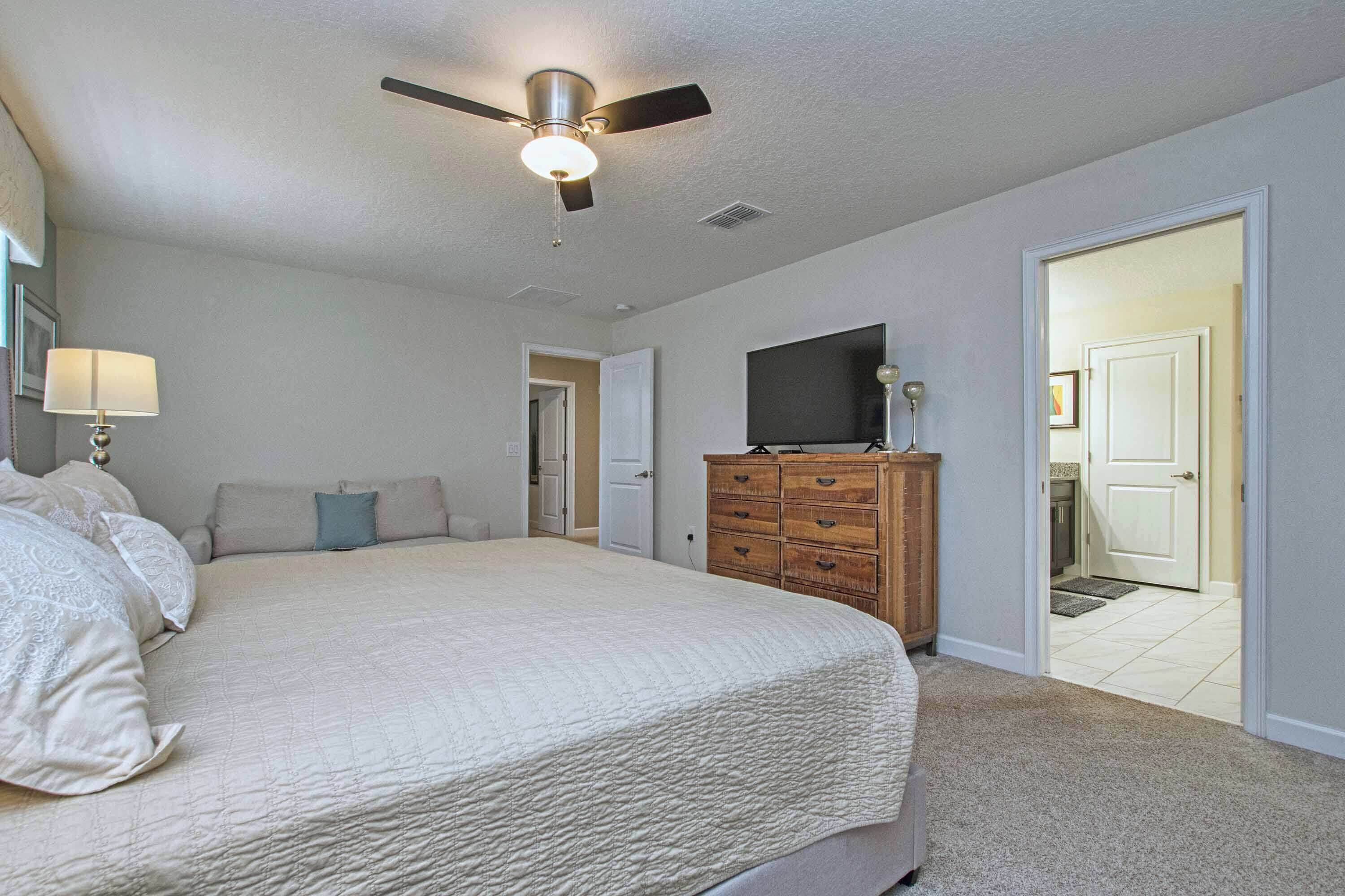 A bedroom with a bed, a dresser, a ceiling fan, and a television.