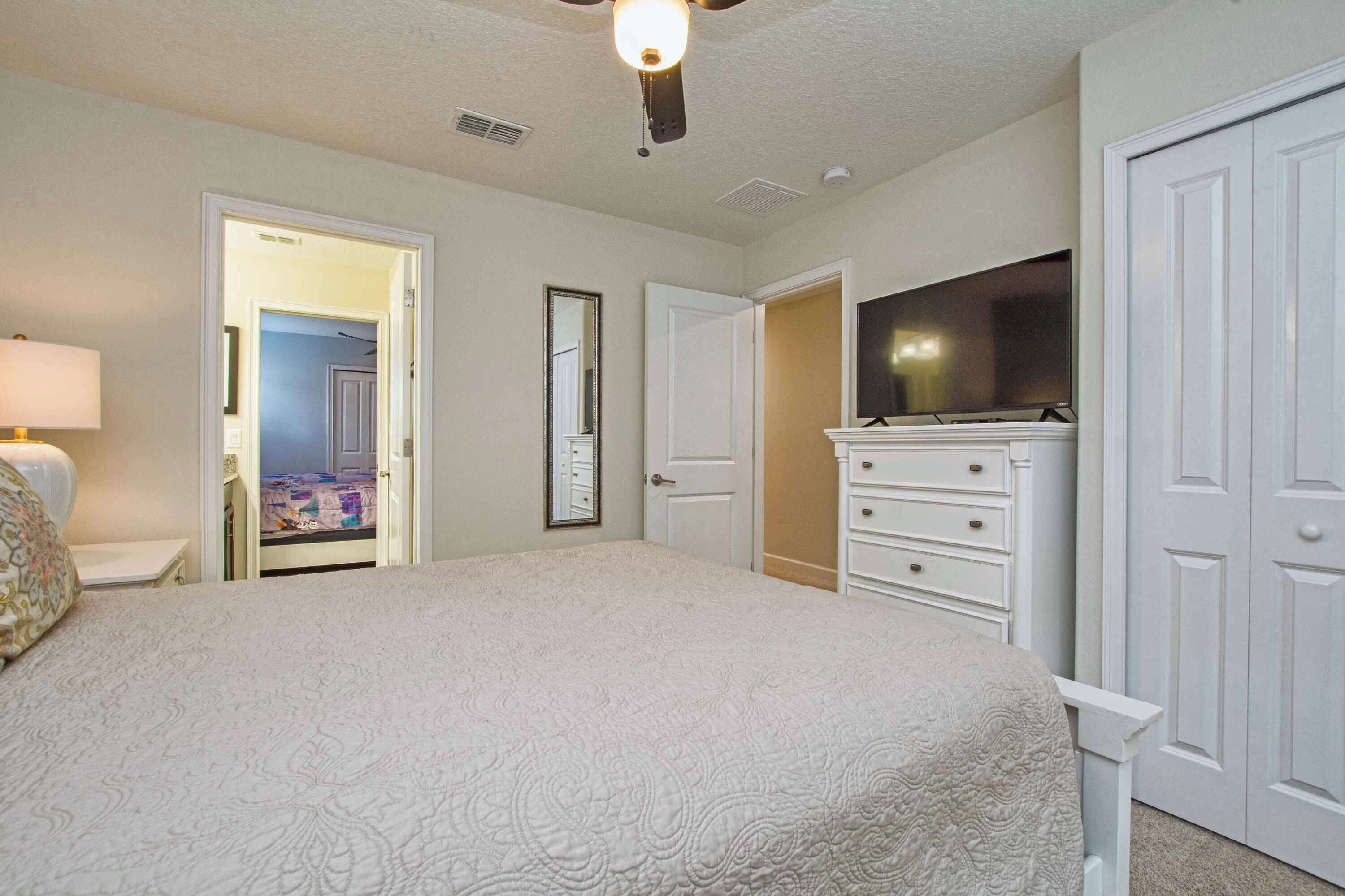 A bedroom with a bed, dresser, television, and a door leading to another room.