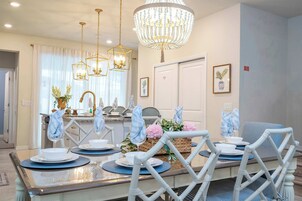 Uma área de refeições com um candelabro, cadeiras brancas e uma mesa posta para quatro pessoas.
