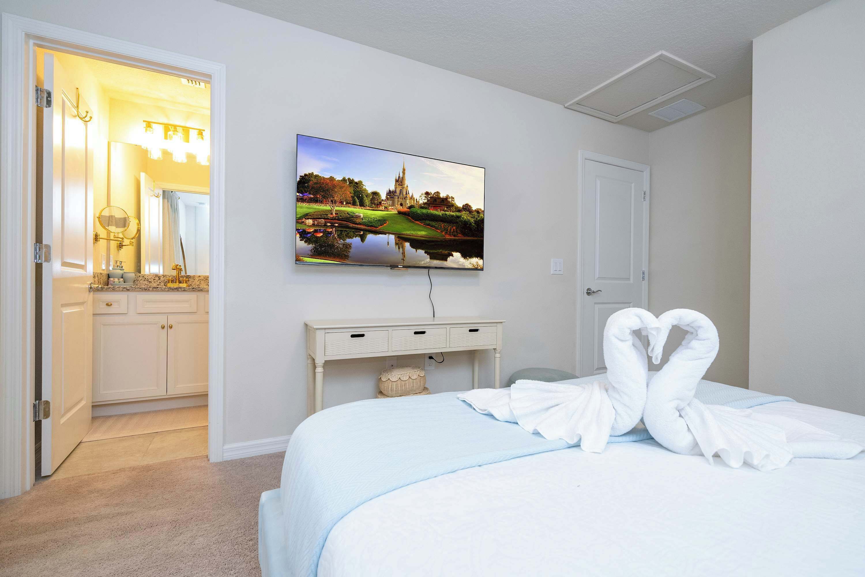A hotel room with a bed, a TV mounted on the wall, a bathroom with a mirror, and a door.