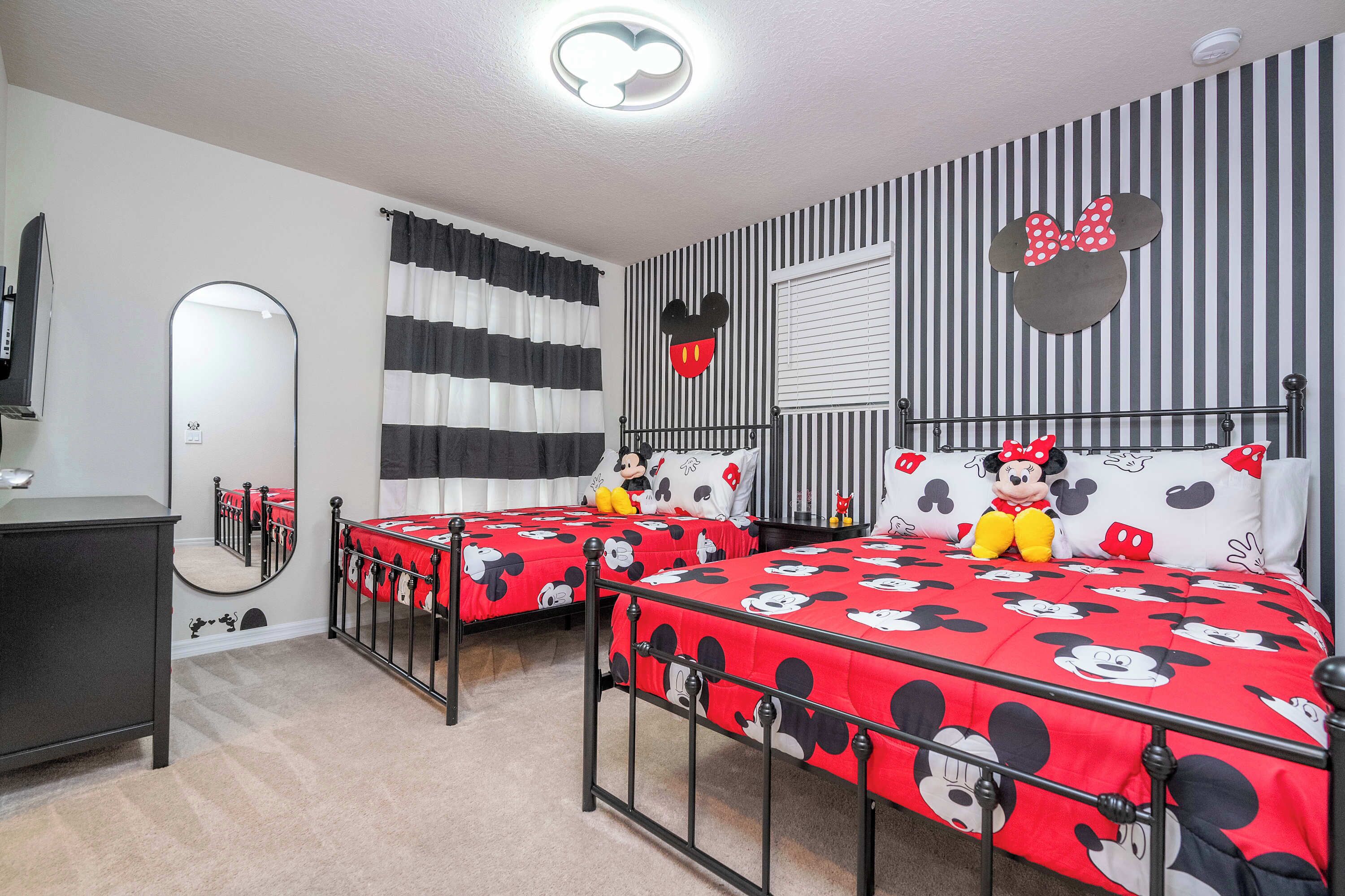 Una habitación con dos camas, un espejo, un tocador y decoración temática de Mickey Mouse.