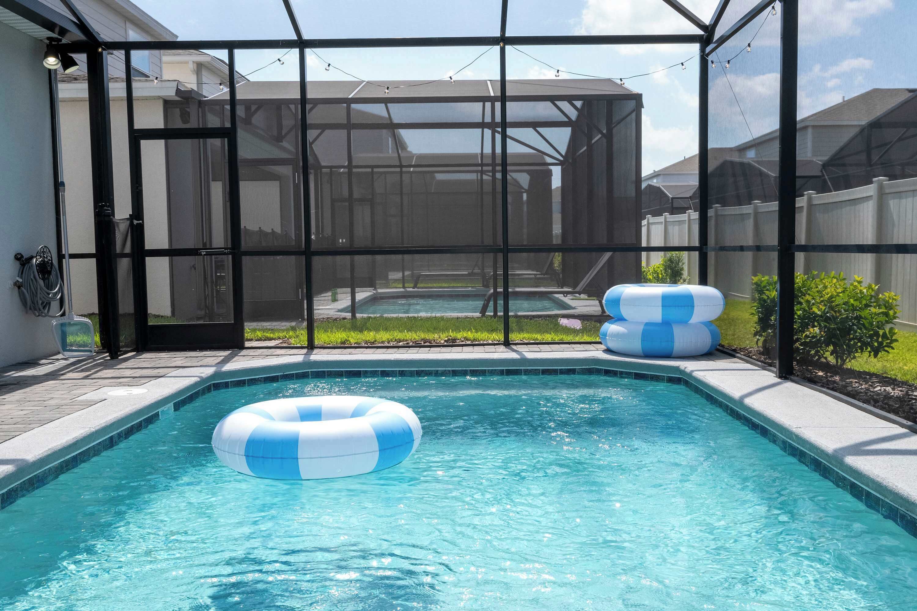 A swimming pool with a glass enclosure, surrounded by a fence, and two inflatable rings.