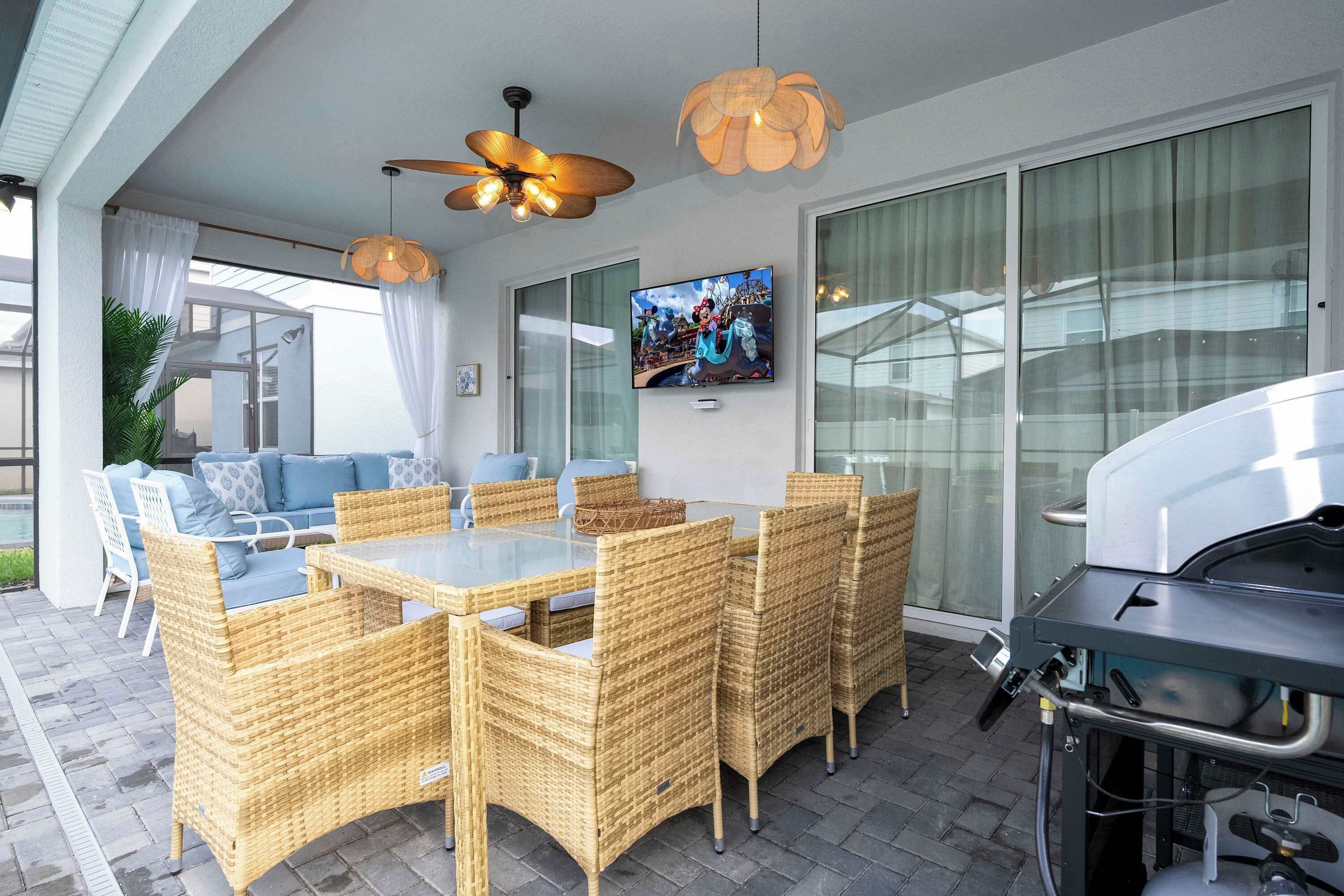 A modern outdoor patio with wicker furniture, a TV, and a grill.