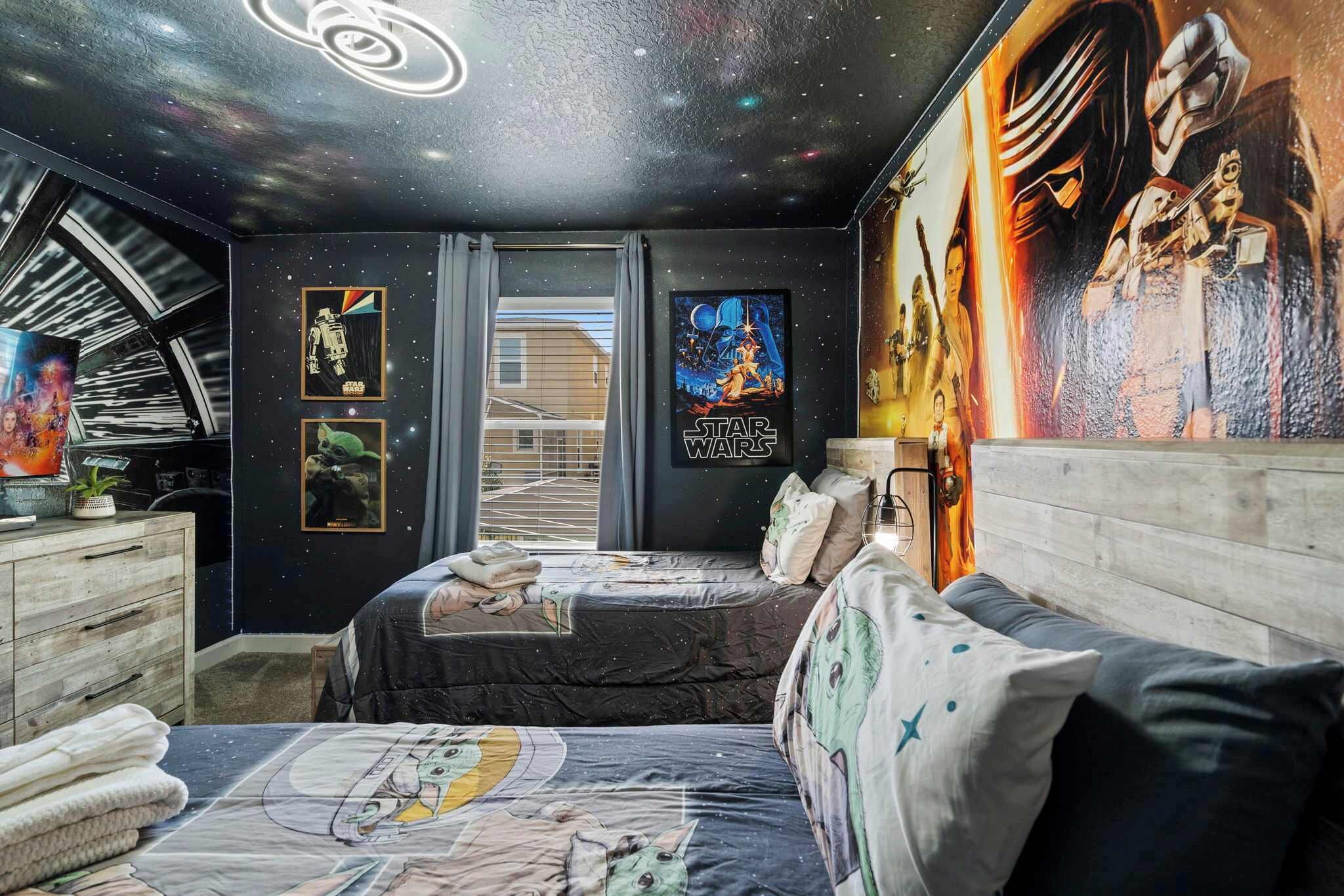 A bedroom with a starry ceiling, a bed with a galaxy-themed bedspread, a dresser, and a wall with Star Wars posters.