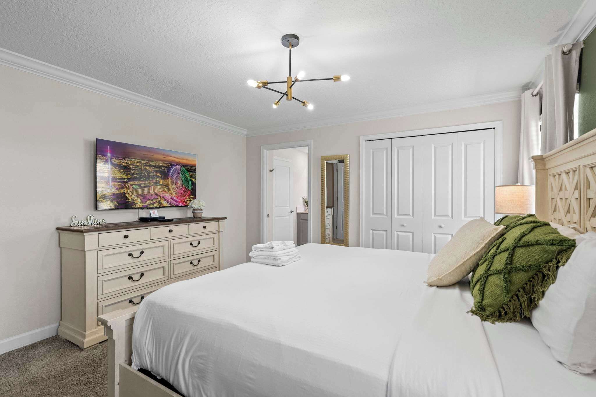 A bedroom with a bed, a dresser, a painting, a mirror, and a door.