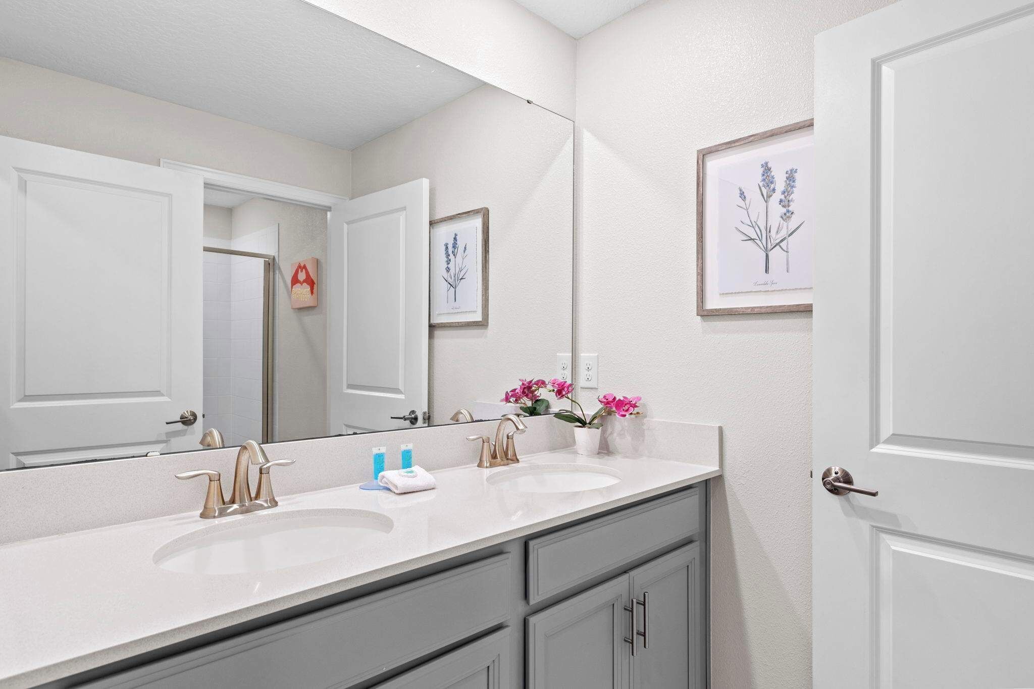 A bathroom with a double sink, a large mirror, and framed botanical prints on the wall.