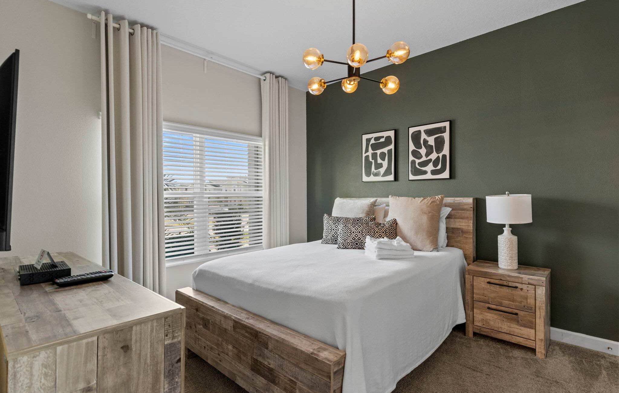 A bedroom with a bed, bedside tables, a lamp, a TV, and a window with blinds.