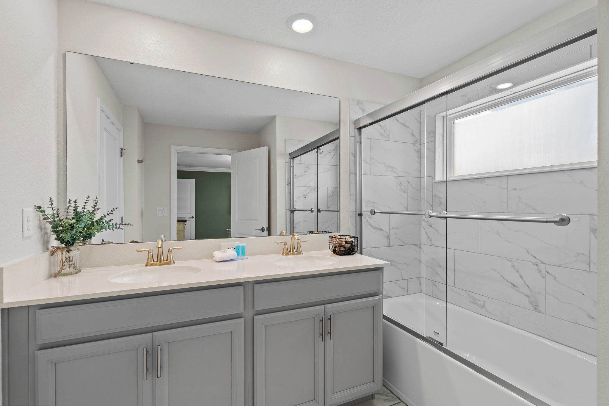 A bathroom with a large mirror, two sinks, a shower with a glass door, and a bathtub.