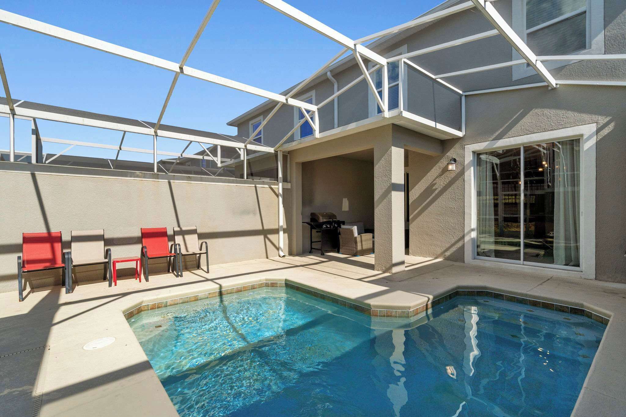 A swimming pool with a covered patio area, outdoor furniture, and a grill.
