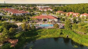 Área residencial com uma casa grande com piscina, rodeada por vegetação exuberante e um pequeno lago.