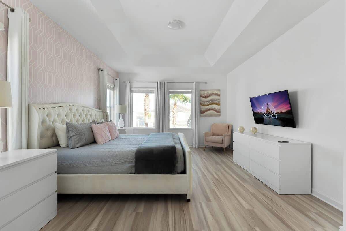 Quarto moderno com cama, televisão, cômoda e cadeira.