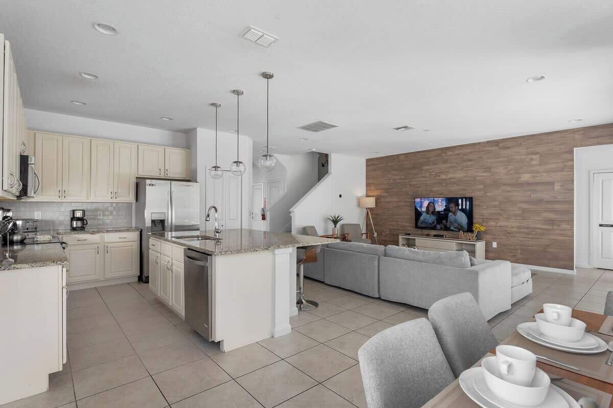 Une cuisine moderne dotée d’un îlot central, un coin repas avec une table et des chaises, et un salon avec un canapé et un téléviseur.