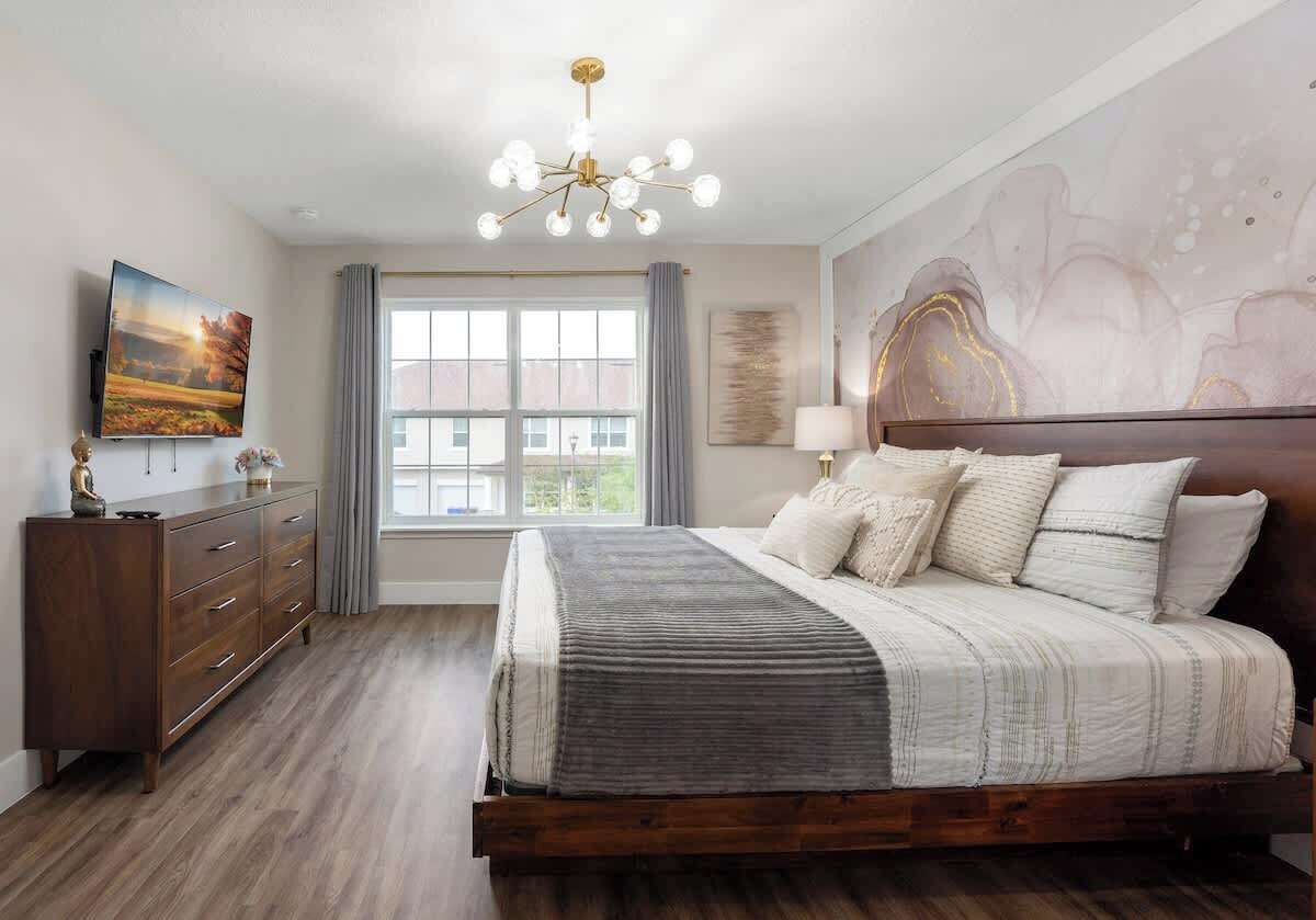 A bedroom with a large bed, a dresser, a TV, and a window with curtains.