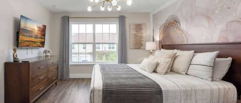 A bedroom with a large bed, a dresser, a TV, and a window with curtains.