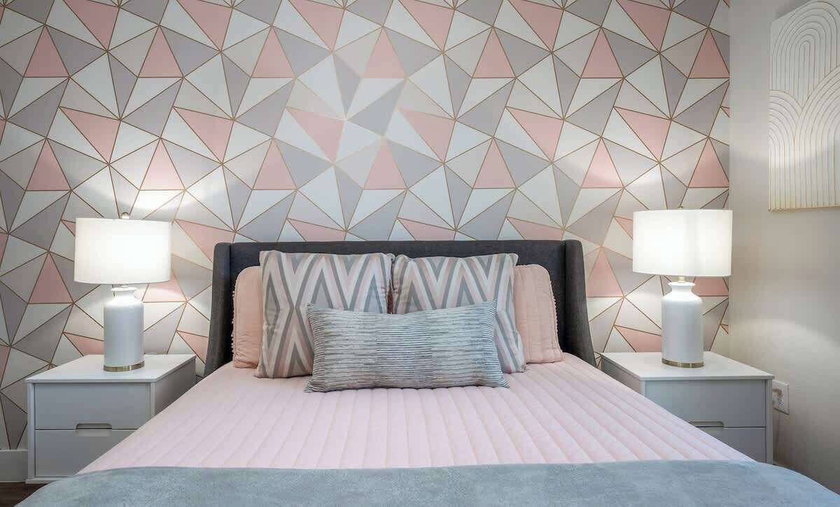 A bedroom with a geometric patterned wall, a bed with multiple pillows, and bedside lamps.