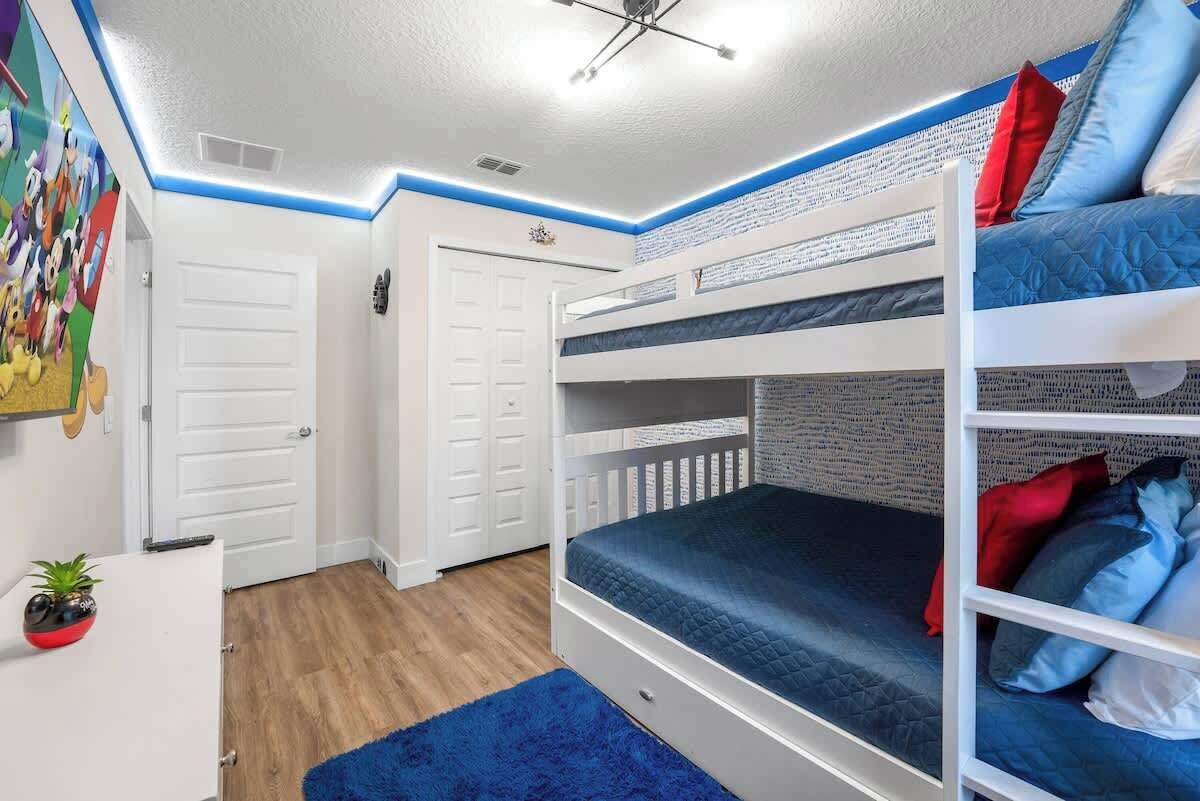 A bunk bed room with a blue rug, white walls, and a ceiling fan.