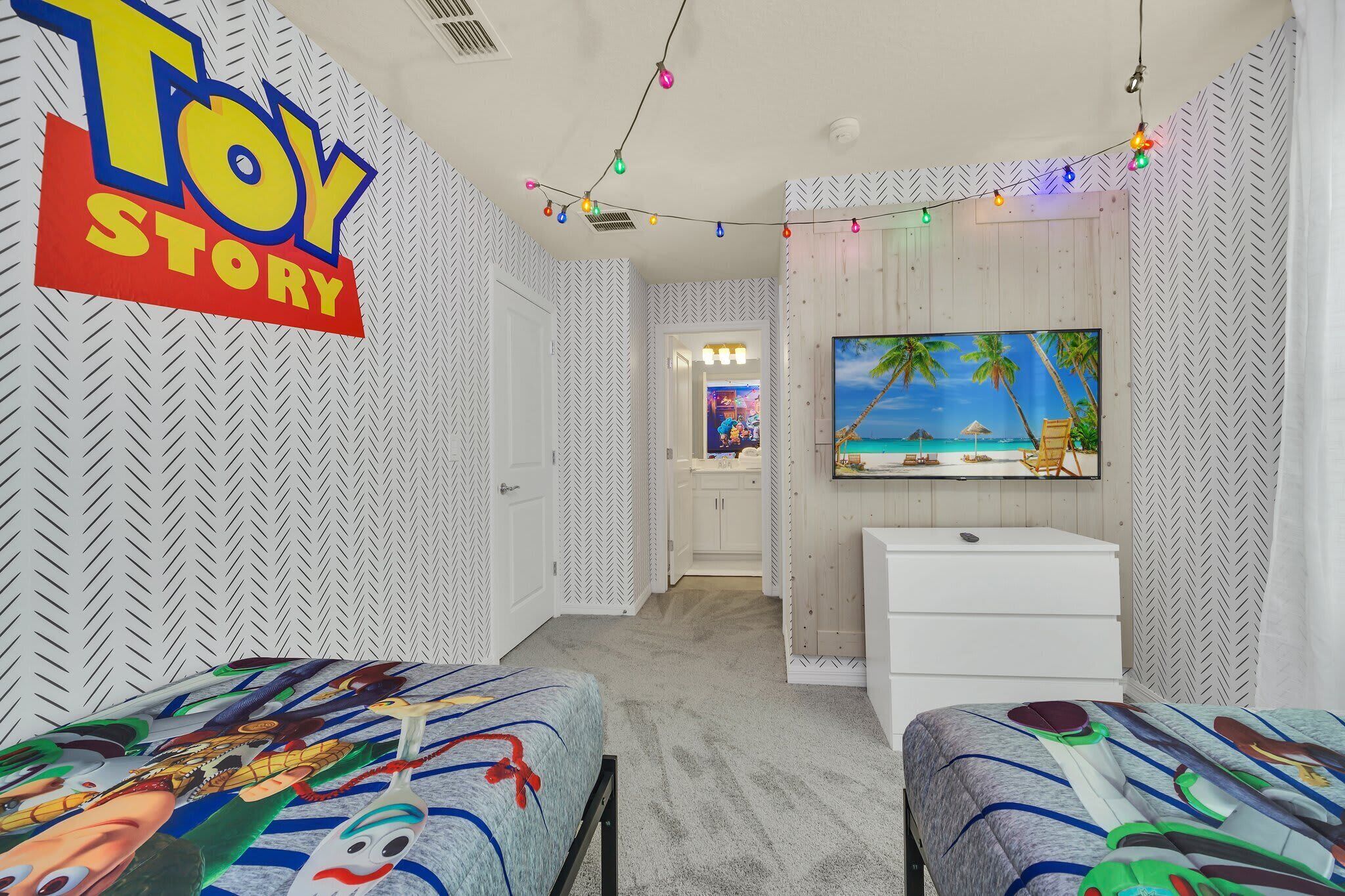 A room with a 'Toy Story' sign, a TV, two beds with colorful bedding, and a herringbone-patterned wall.