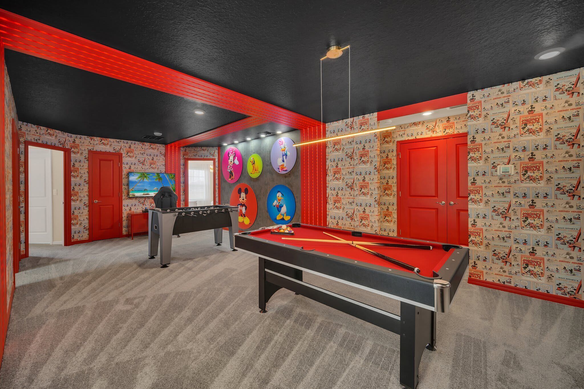 Een pooltafel met een rode viltkleed, een tafelvoetbaltafel en een televisiescherm.
