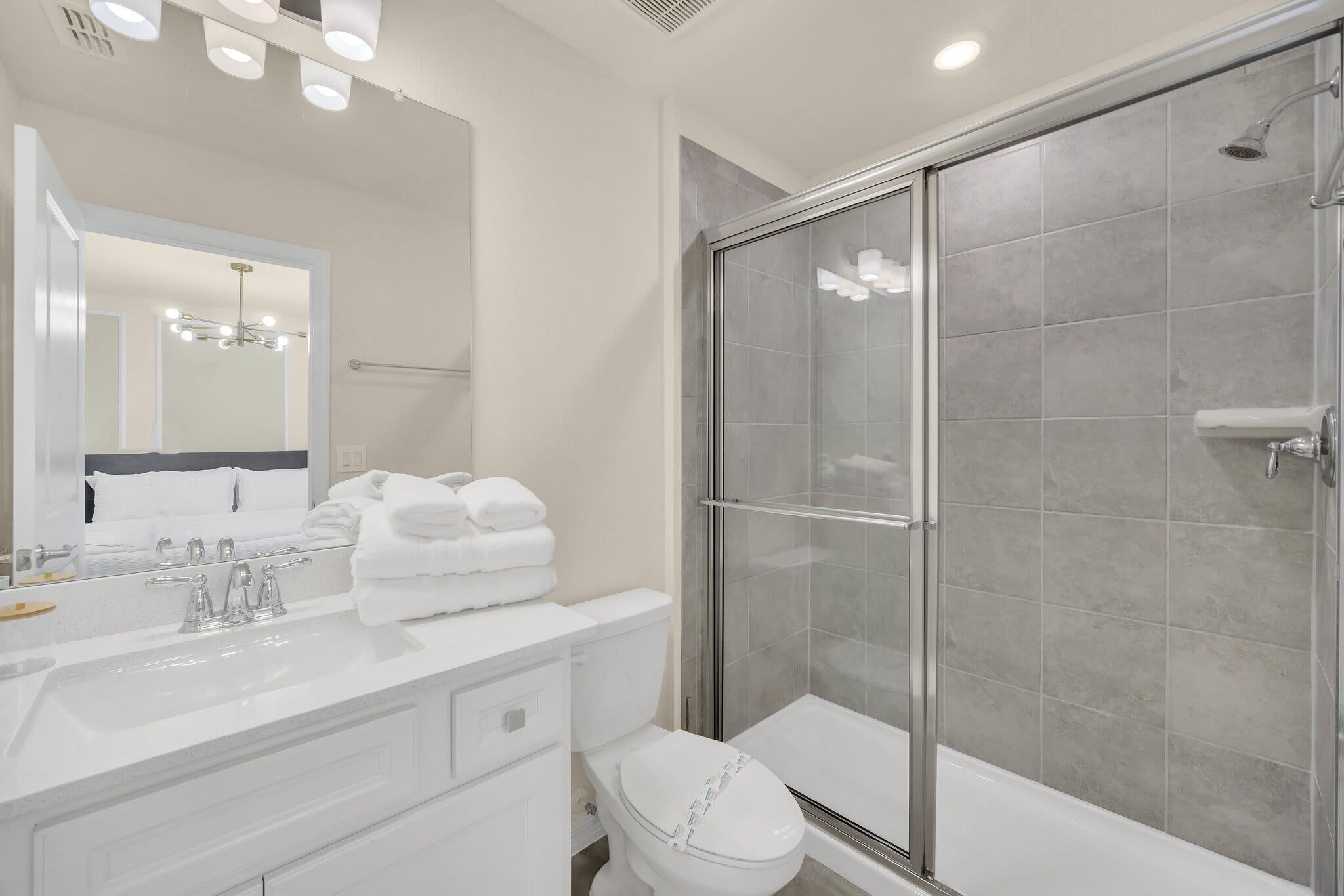 A modern bathroom with a glass-enclosed shower, a white sink with a mirror, and neatly stacked towels.