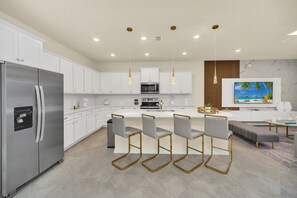 A modern kitchen with white cabinets, stainless steel appliances, and a central island with bar stools. - Chic 10br Retreat With Themed Rooms & Pool (Clermont)