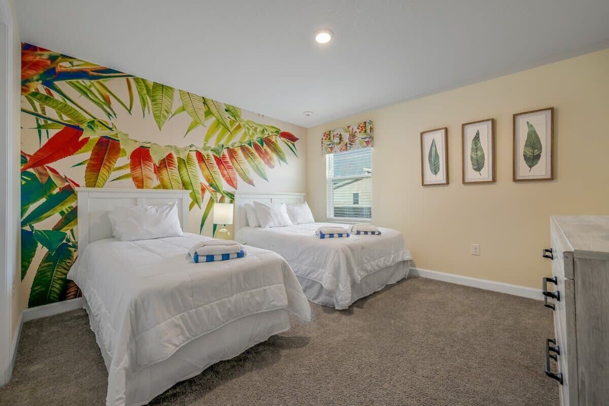 A hotel room with two beds, a large tropical mural, and three framed leaves on the wall.
