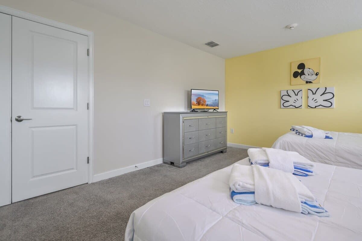 Une chambre avec deux lits, un téléviseur posé sur une commode et un tableau de Mickey Mouse accroché au mur.
