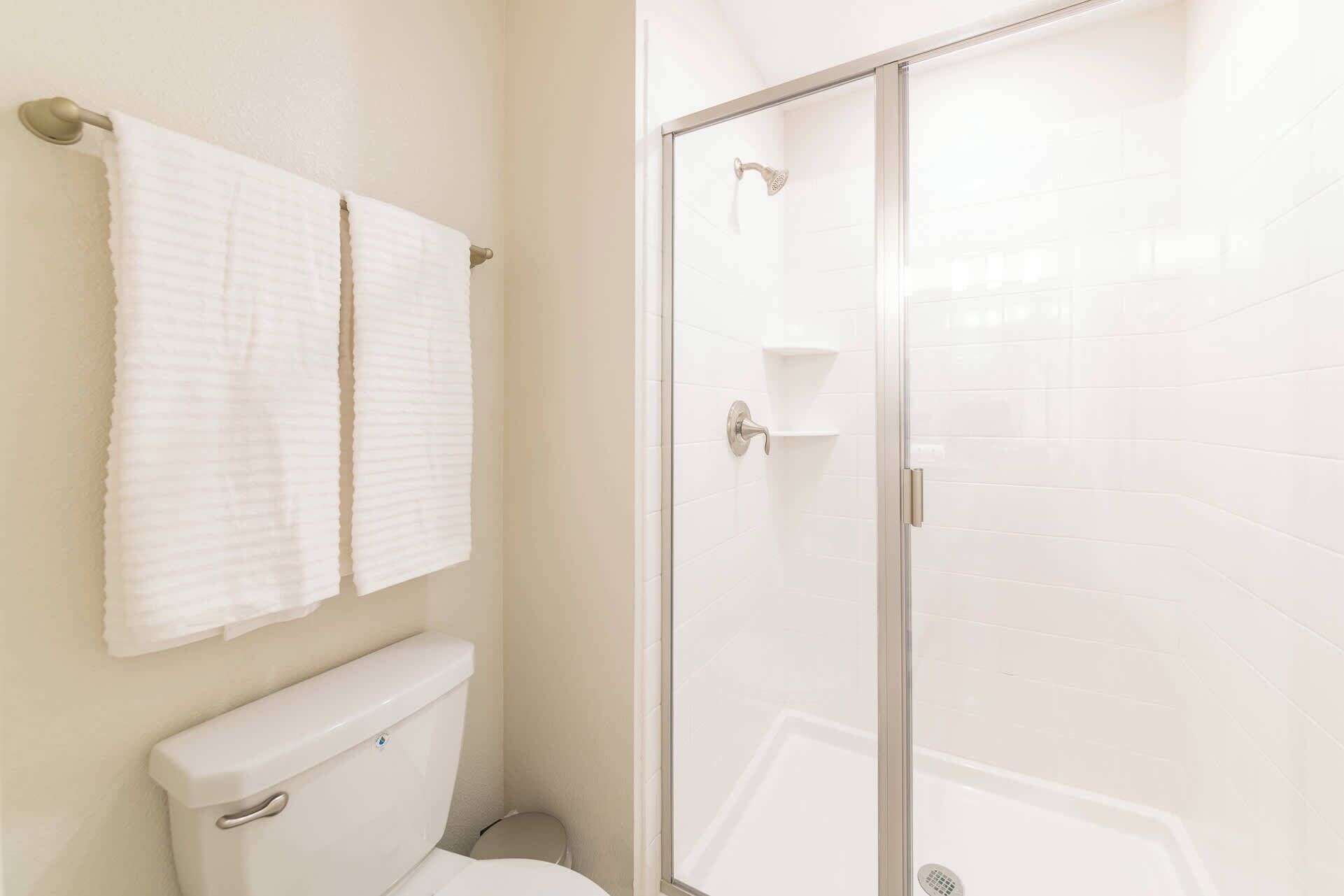 A bathroom with a toilet, a shower with a glass door, and two white towels hanging on a towel rack.