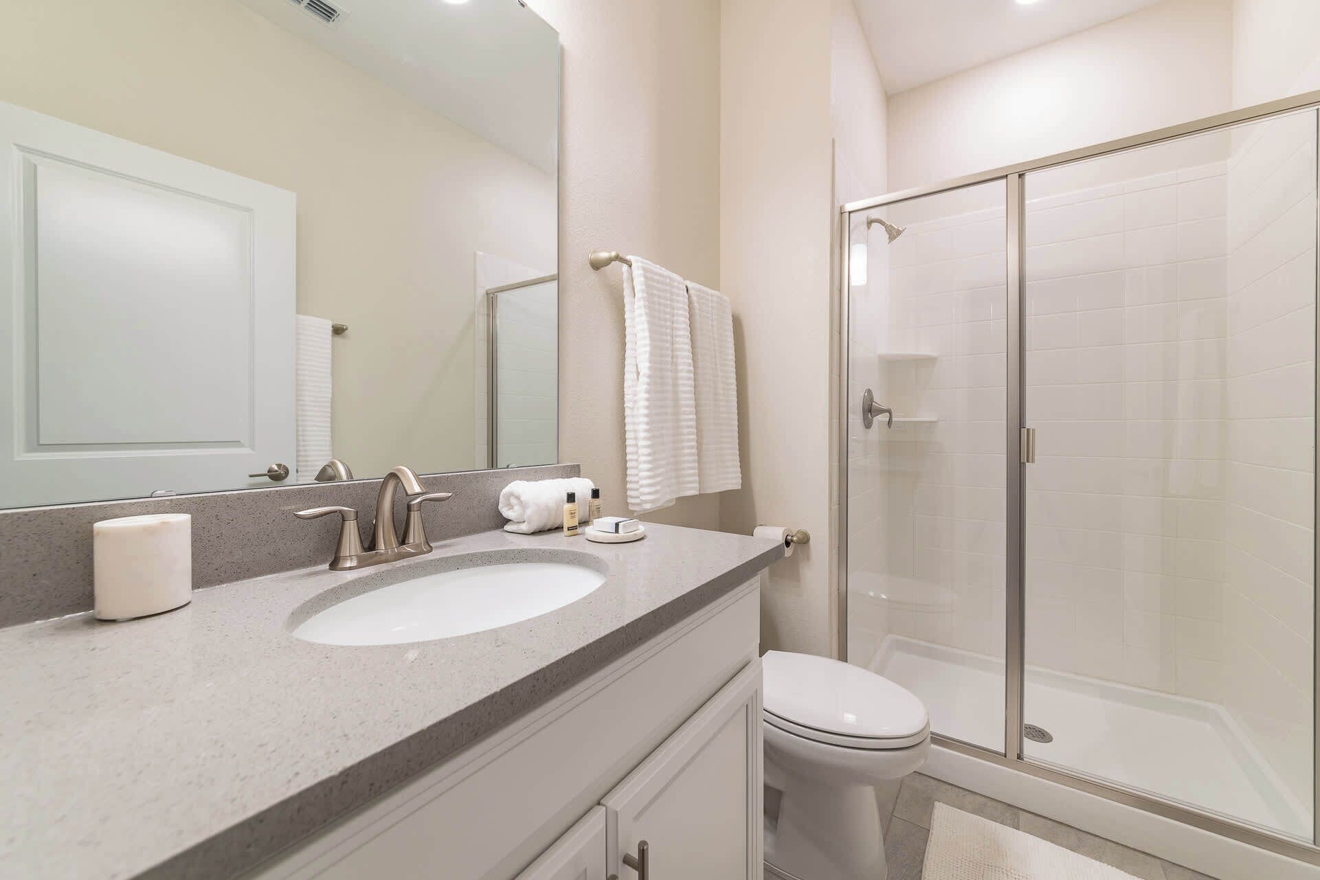 A bathroom with a sink, mirror, towel rack, toilet, and a glass-enclosed shower.