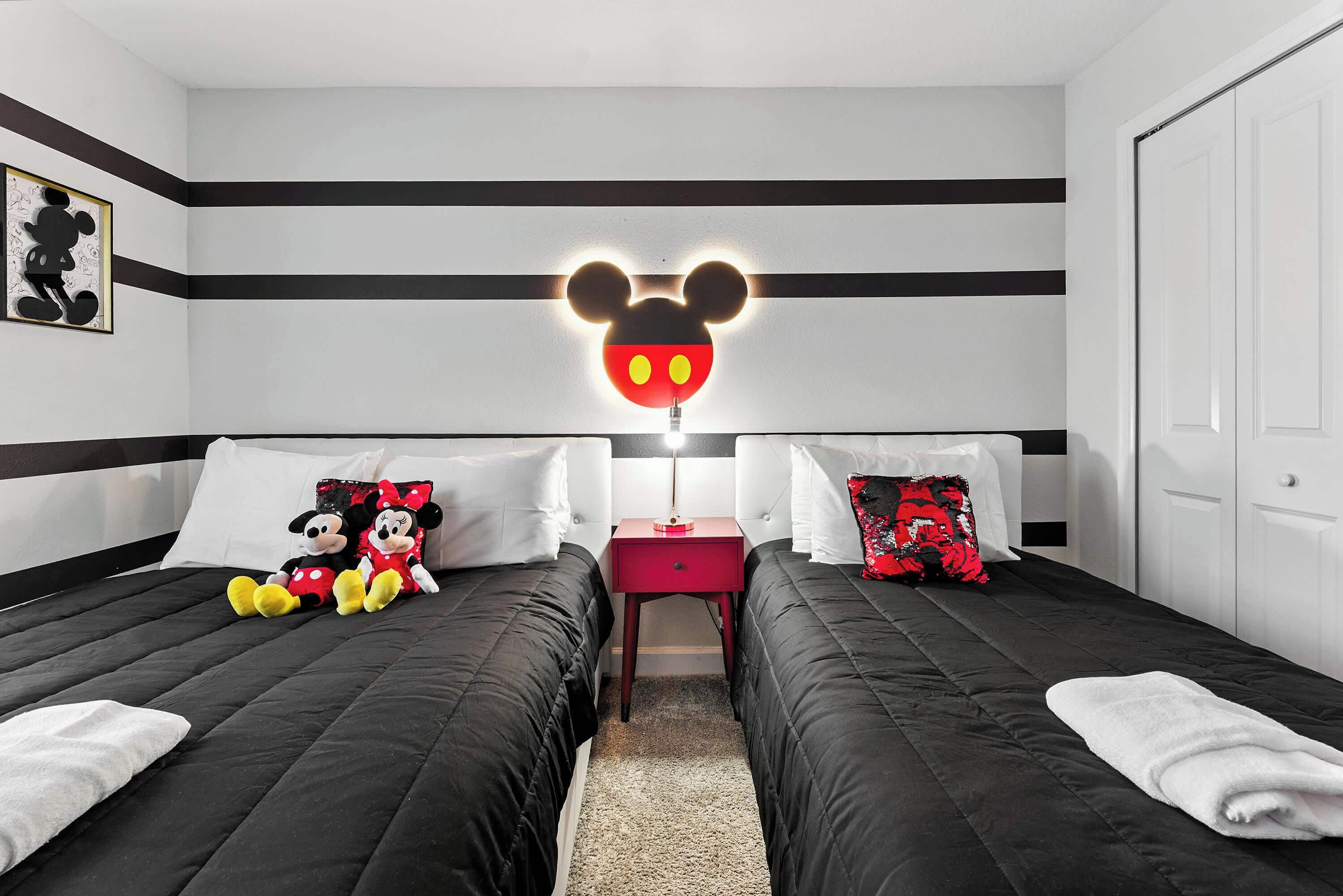 A hotel room with two beds, a Mickey Mouse light, and two Mickey Mouse plush toys.